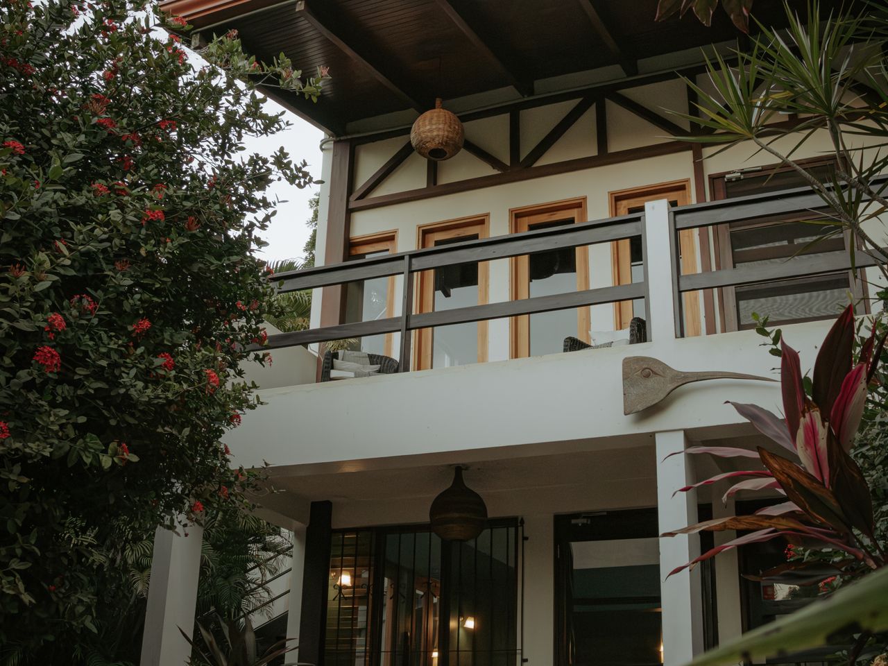 Two-story tropical home with a balcony among gardens